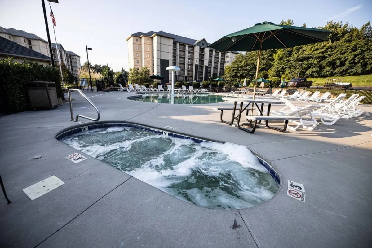 An inviting exterior pool and hot tub area with lounge chairs, outdoor tables, umbrellas, and a cheerful, social atmosphere. This communal space is ideal for guests to relax after exploring the area or to gather for evening social activities.