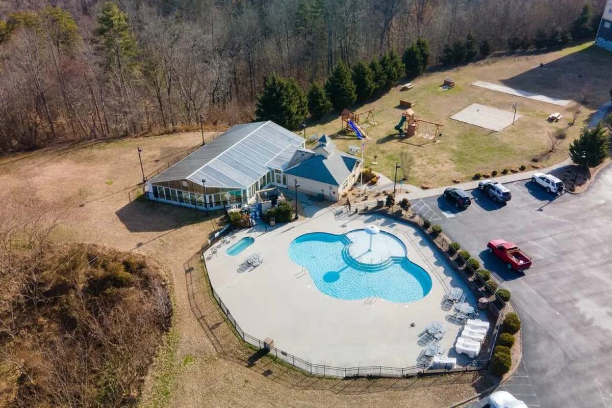 An exterior view featuring a sparkling swimming pool surrounded by trees, with a recreational area and visible playground equipment nearby. The atmosphere is lively and joyful, suggesting family fun and outdoor enjoyment.