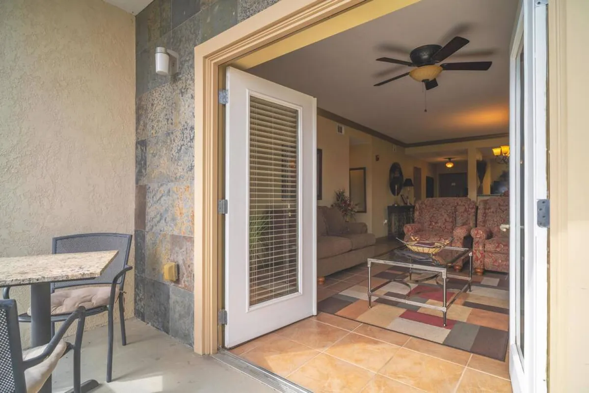 A welcoming scene with an open door leading to a patio area featuring comfortable chairs and a table setting, hinting at indoor-outdoor flow. The inviting setup suggests easy access for all guests to enjoy communal or relaxation spaces.