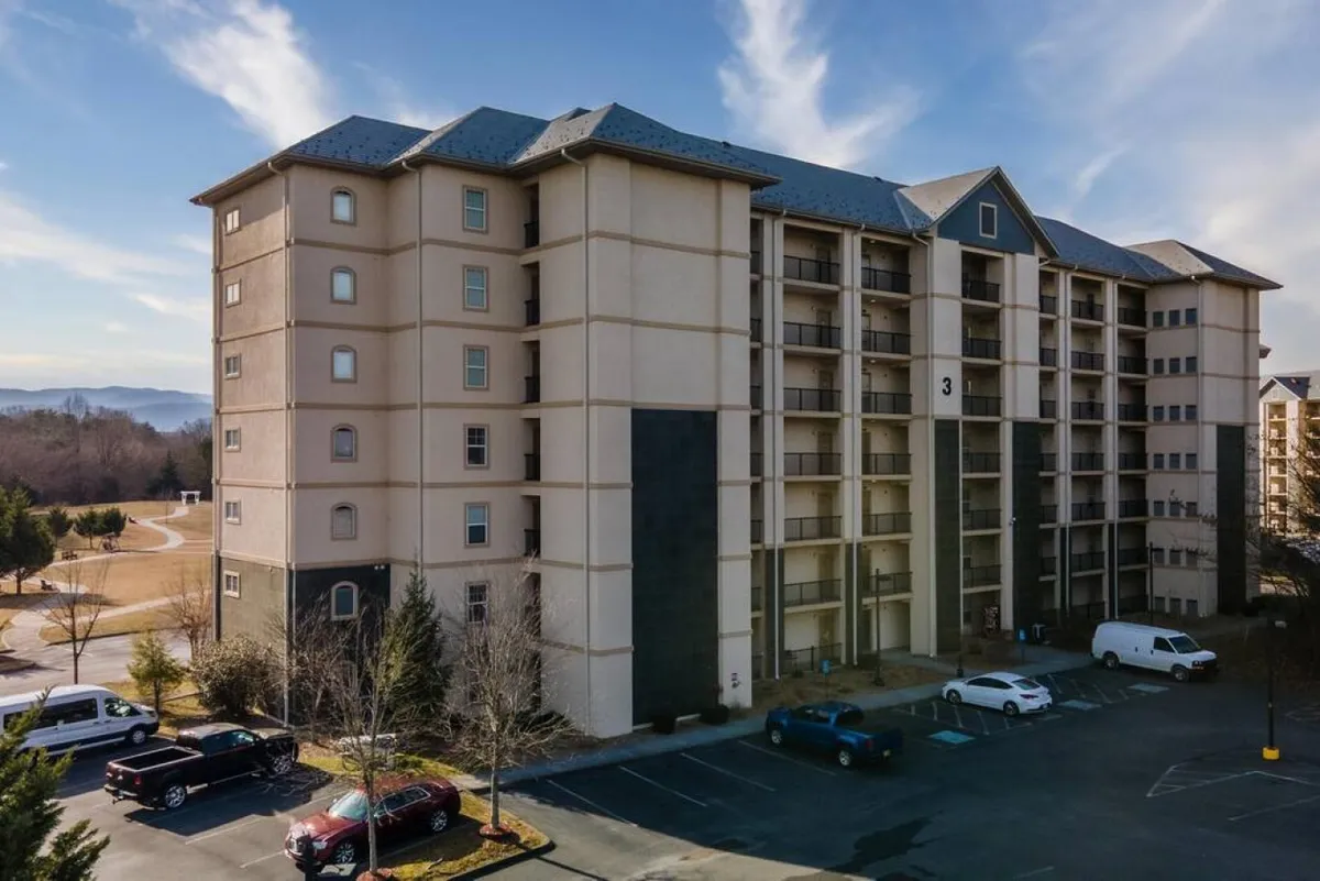 The multi-story condo building with landscaped surroundings and a welcoming parking area, set against a pleasant backdrop. This exterior shot situates the property within its lively, accessible environment, hinting at walkability and proximity to attractions.