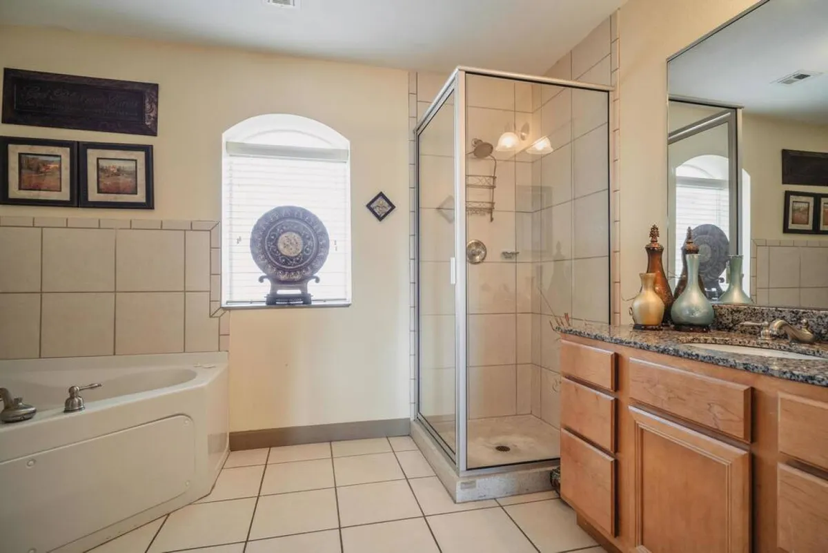 A modern, serene bathroom featuring a freestanding garden tub, a glass shower enclosure, granite countertops, and decorative wall art. The light and airy space evokes relaxation and convenience.