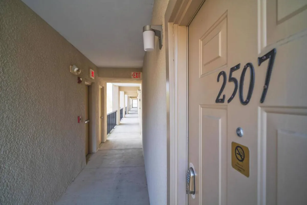 This image captures the entryway to one of the condo units, with a prominently marked door number, a light fixture, and a visible exit sign in a well-lit hallway. The area appears easy to navigate, suggesting step-free access and clear signage.