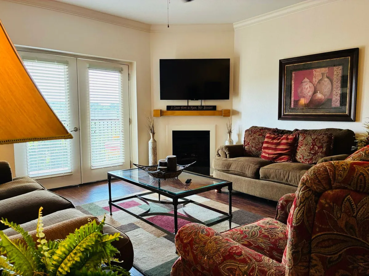 A comfortable living area featuring a sofa, coffee table, television, and sliding glass doors that invite in natural light. A table lamp adds warmth, and the arrangement encourages both relaxation and group interaction, with easy access to outdoor views.